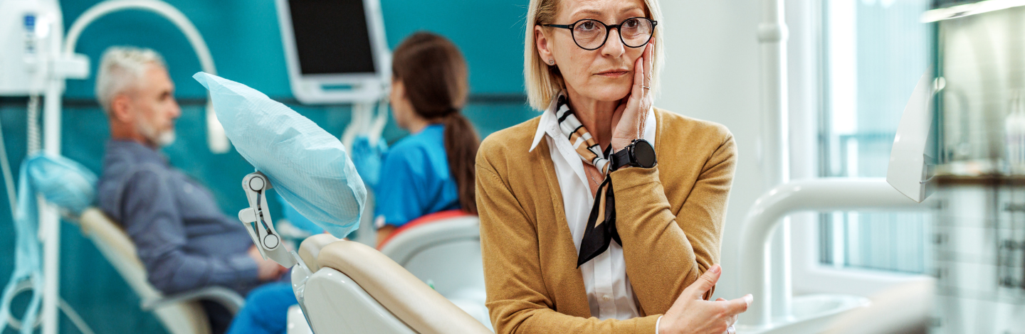 older woman holds face in pain at dental office