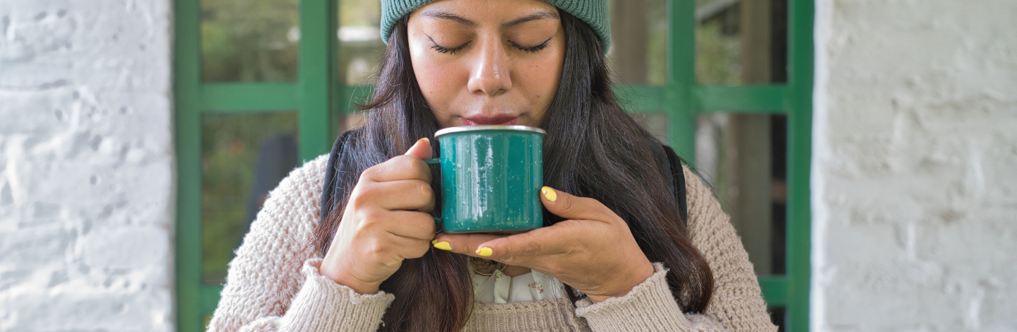 Woman holds warm mug of coffee or tea to face