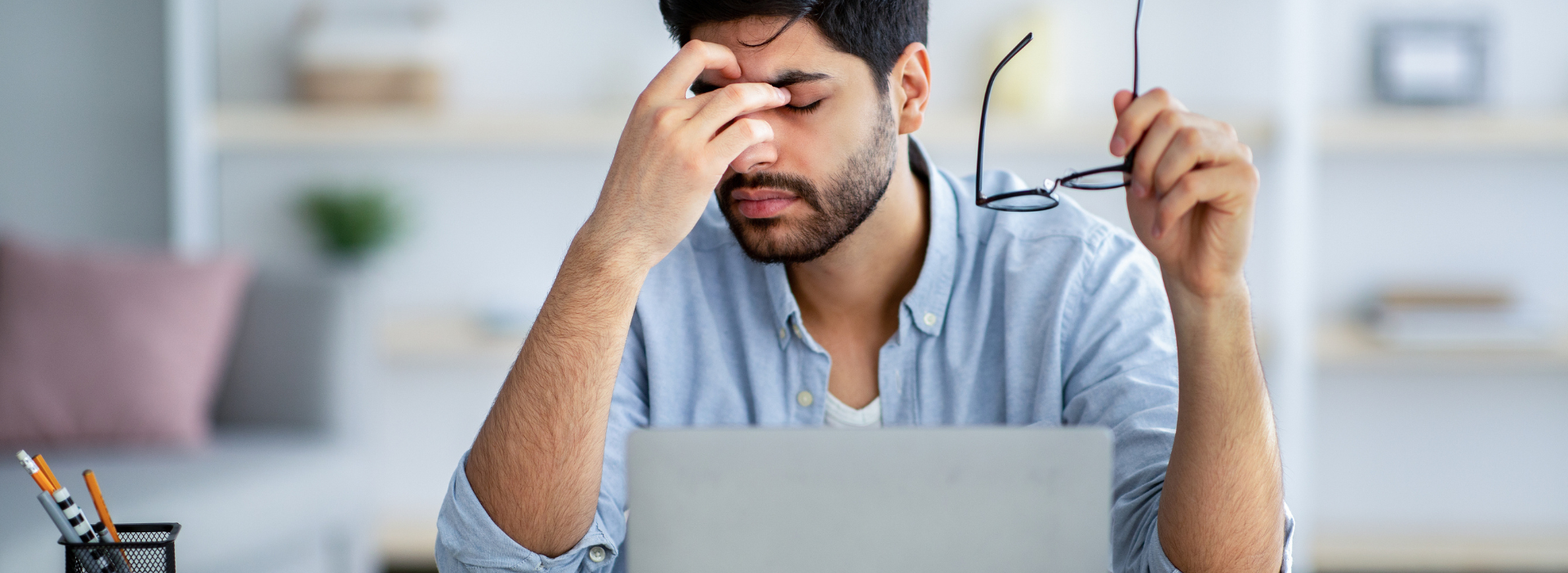 Man rubs head from eye strain while looking at laptop