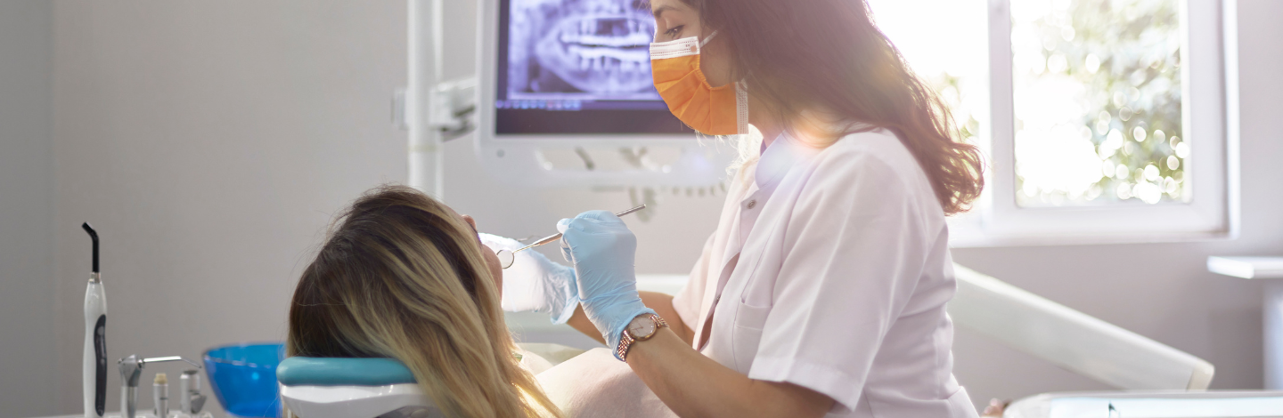 Dentist woman in an orange mask working on the teeth in her patient's mouth