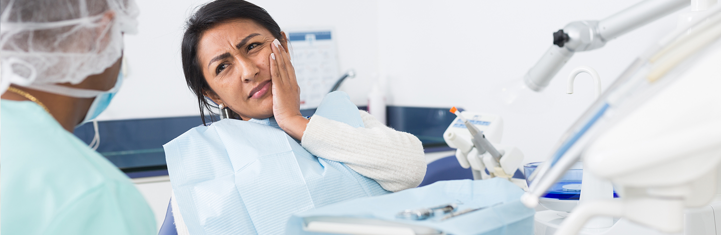 Woman holds side of face in pain at the dentist