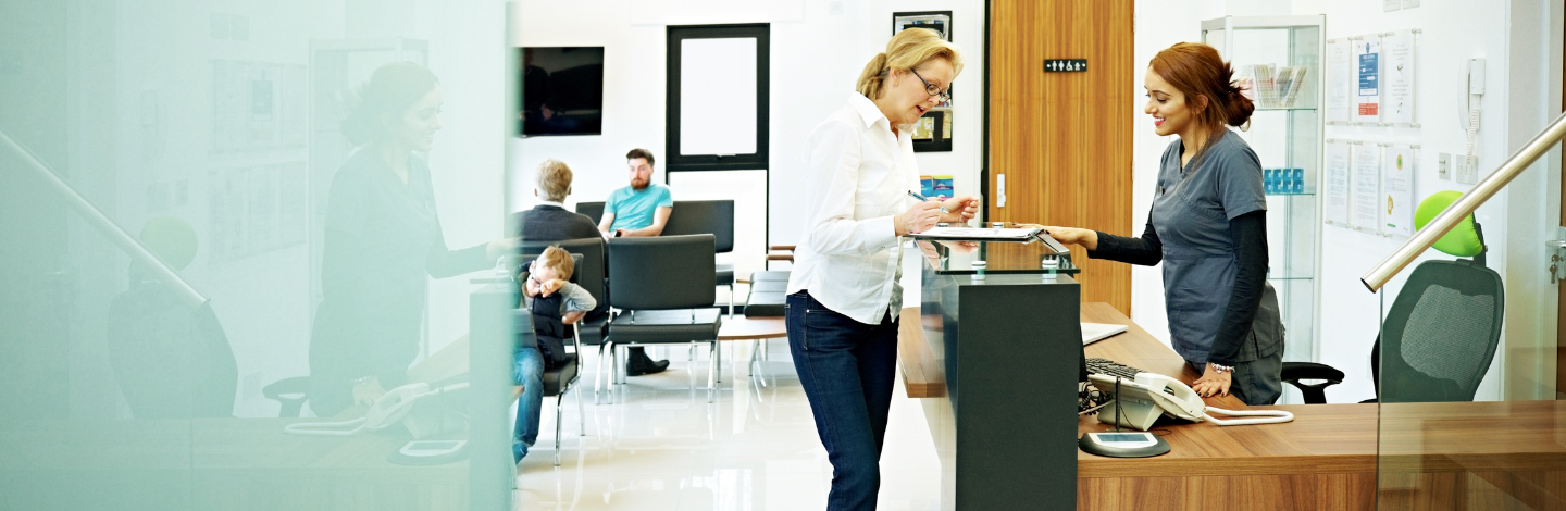 Woman standing at the reception desk in a dental clinic filling out the papers