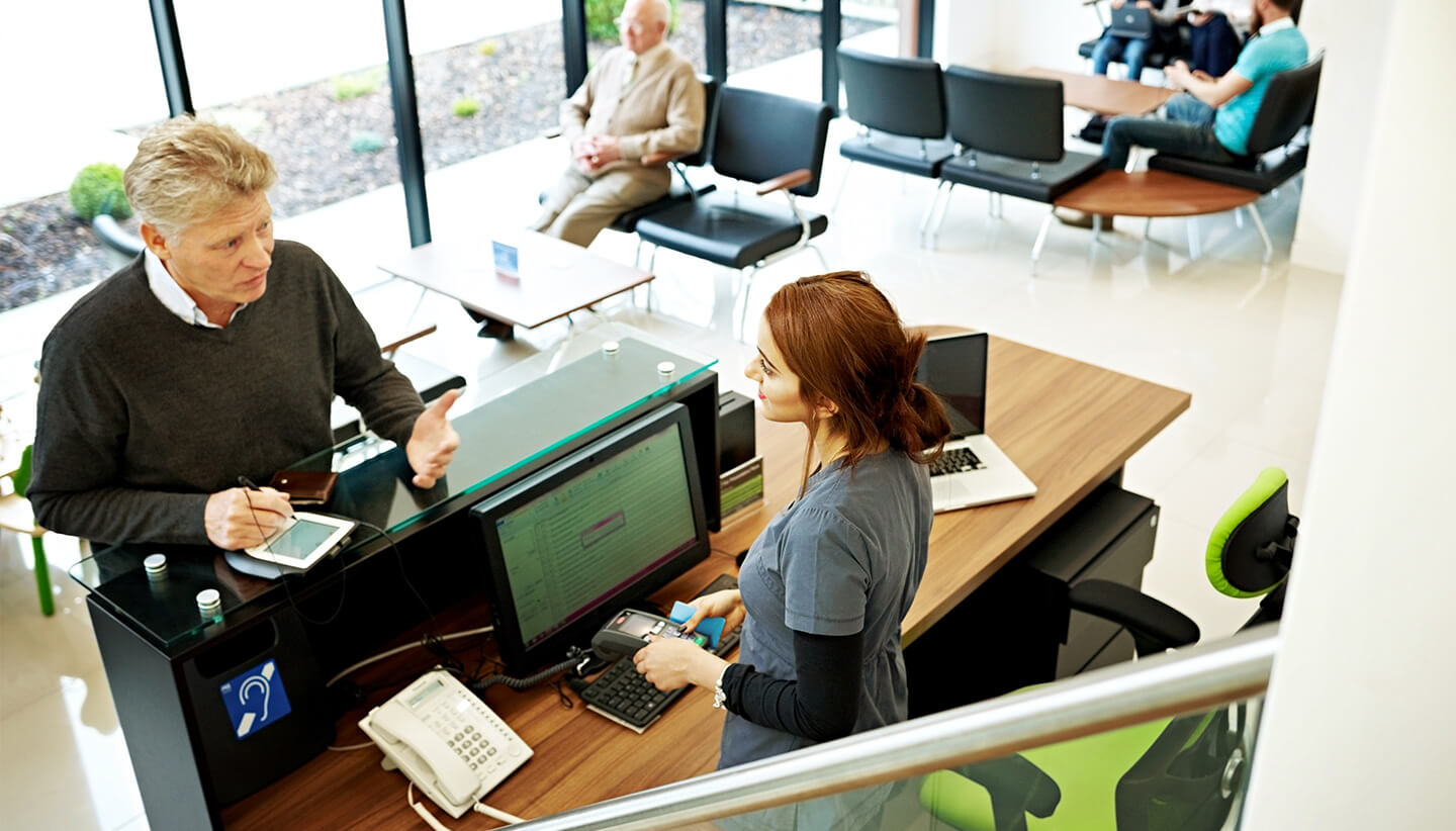 Patient talking with receptionist at dentist 1440x830