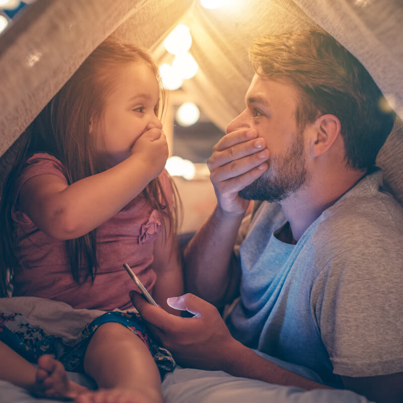 dad-and-daughter-covering-mouths-in-fort-800x800